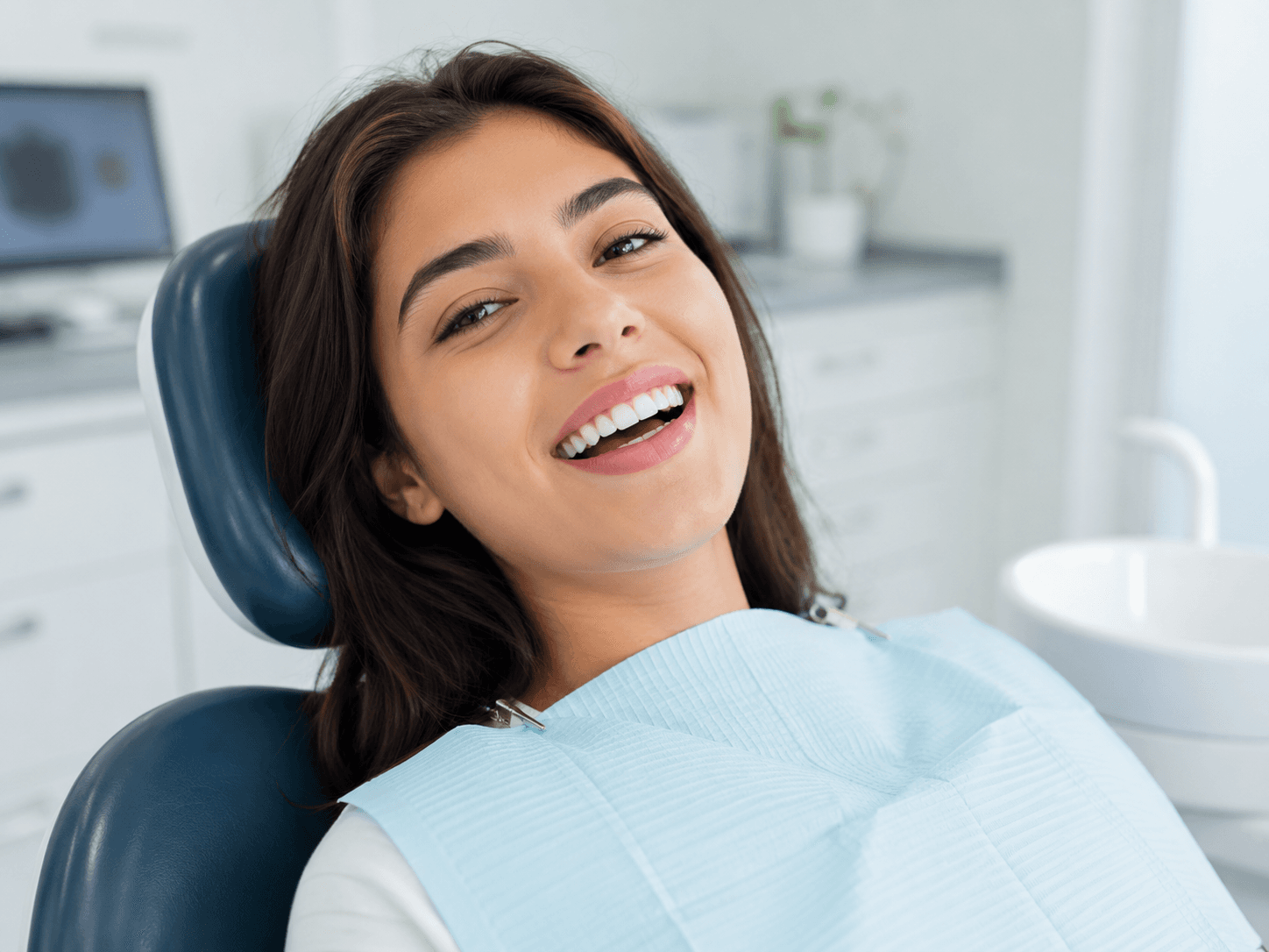 Paciente sonríe recostada en el sillón dental después de una limpieza