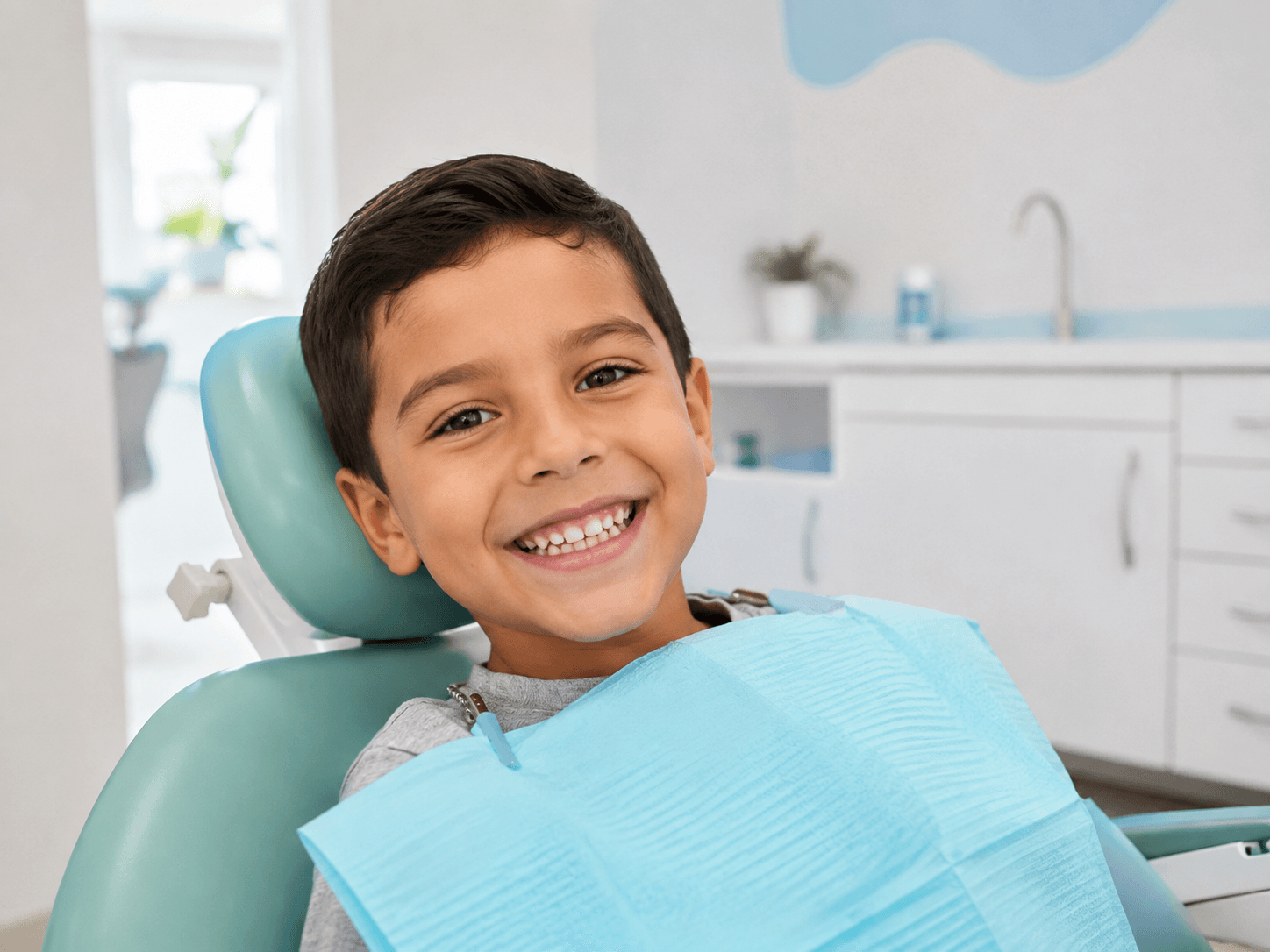 Niño sonriente sentado en el sillón dental con el babero de protección puesto